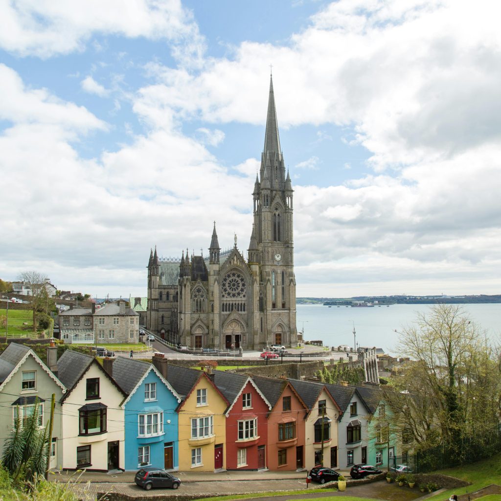 Picturesque St. Colman's Cathedral overlooking colorful houses and sea in Cobh, Ireland.