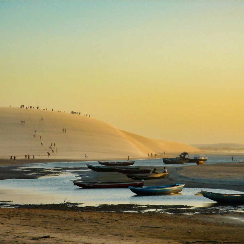 Stunning sunset view of boats and sand dunes at Jericoacoara Beach, Brazil.